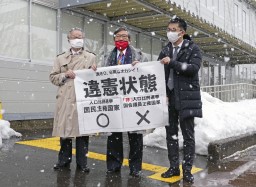 　衆院選の「１票の格差」訴訟の判決を受け、仙台高裁秋田支部前で「違憲状態」と書かれた紙を掲げる弁護士＝１５日午後