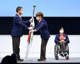 　北京冬季パラリンピック日本選手団の結団式で、河合純一団長（左）から団旗を受け取る旗手の川除大輝。右は主将の村岡桃佳＝２４日午後、東京都新宿区