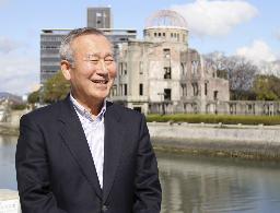 　原爆ドーム（後方右）のそばで、インタビューに答える秋葉忠利氏＝２０２０年２月、広島市