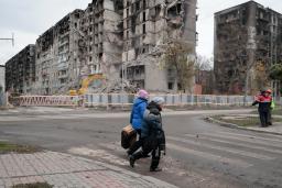　４日、ウクライナ東部ドネツク州マリウポリで、戦闘で破壊された建物の前を歩く人たち（ＡＰ＝共同）