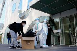 　新型コロナ対策で封鎖されたオフィスビルから防護服姿で荷物を運び出す担当者ら＝２１日、北京（共同）
