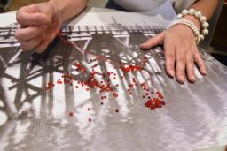 　ビーズを縫い付け、朝鮮人虐殺を表現する金暎淑さんの作品＝７月３１日、東京都品川区