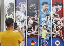 　バスケットボール男子Ｗ杯の広告の前で写真を撮るドイツ人観光客。「日本戦を楽しみにしている」と話した＝２４日、那覇市