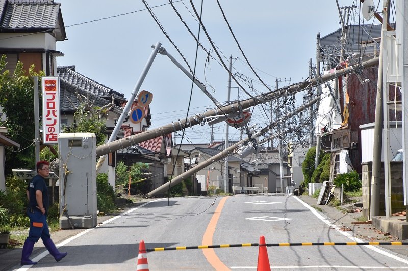 連なるようにして反対側の民家に倒れ込む電柱＝９日午前１１時半ごろ、館山市船形