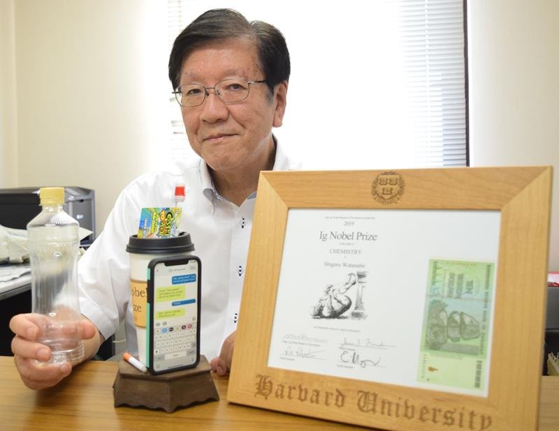 イグ・ノーベル賞で受賞したトロフィーなどを前に、研究で突き止めた５歳児の唾液量と同じ５００ミリリットルのペットボトルを手に取る渡部教授＝浦安市の明海大
