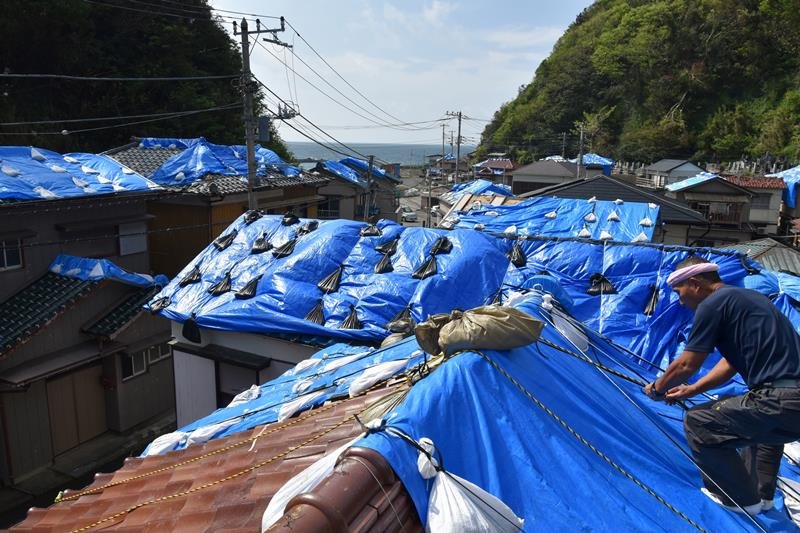ブルーシートが風に飛ばされないように土のうを取り付ける久保田さん＝８日午前１０時４５分、鋸南町岩井袋