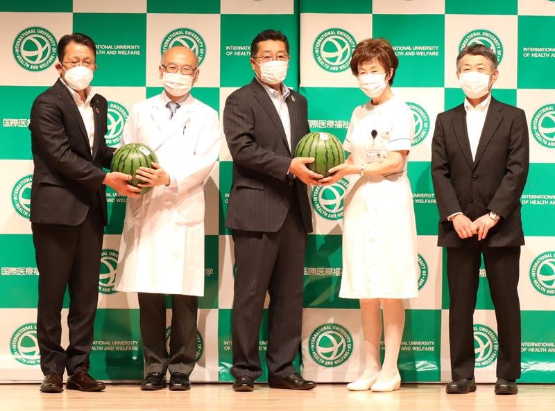 山崎予防医学センター長（左から２人目）にスイカを手渡す五十嵐市長（左）ら＝成田市の国際医療福祉大学病院
