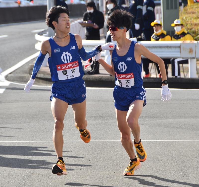９区の野村優作（右）にたすきを渡す順大８区の津田将希。区間賞を獲得した＝横浜市戸塚区
