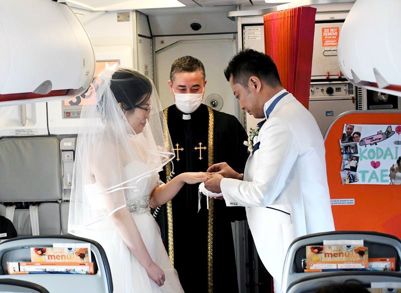 飛行中の機内で、妻の妙さん（左）に結婚指輪をはめる晃大さん
