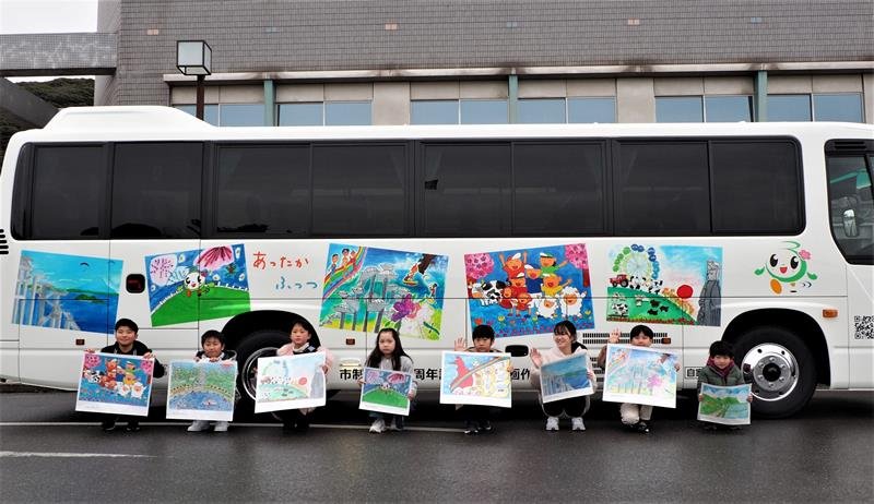 ラッピングバスの前で採用された自分たちの絵を手に記念撮影する児童＝富津市
