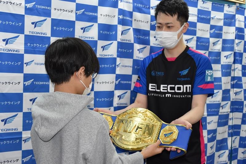 テックウイング代表（右）からチャンピオンベルトを受け取るこうちゃん（左）＝千葉市中央区
