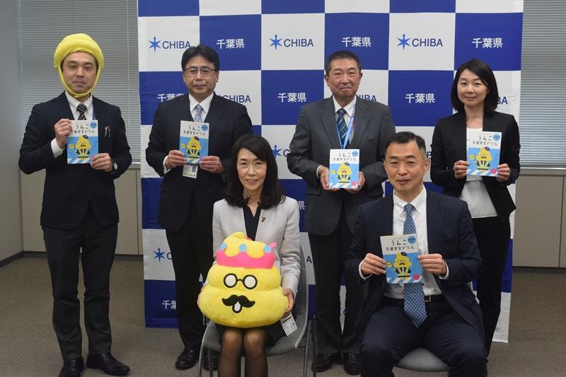 うんこドリル寄贈式の記念撮影で人気キャラクター「うんこ先生」を手に持つ冨塚教育長（前列左）とトヨタ・モビリティ基金関係者ら＝１８日、千葉県庁