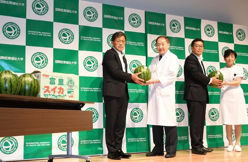 五十嵐市長（左）から旬のスイカを受け取る宮崎病院長（左から２人目）ら＝成田市
