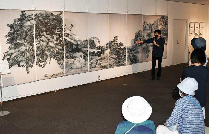 原爆の図の第３部「水」について、「川にたどり着いた途端に息絶えた人が多く描かれている」などと解説する岡村さん＝１２日、成田市
