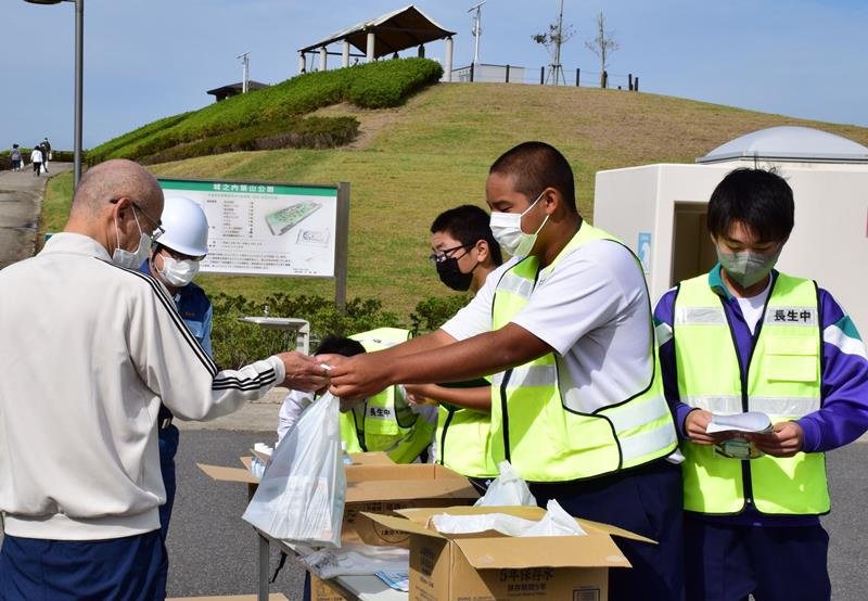 訓練で標高１０メートルの築山に避難した住民に、非常食を配る防災部の生徒＝長生村
