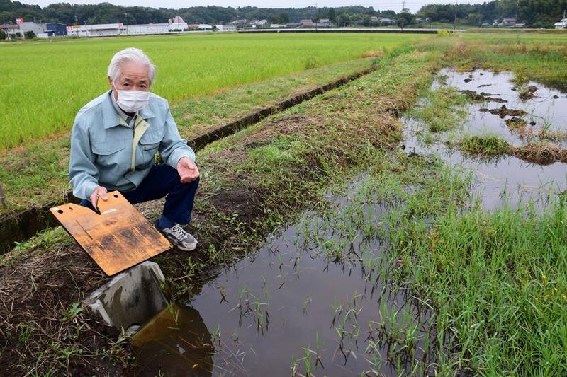 田んぼダムの仕組みを説明する鶴岡会長。調整板をはめると水田から流れ出る水量を抑えられる＝茂原市
