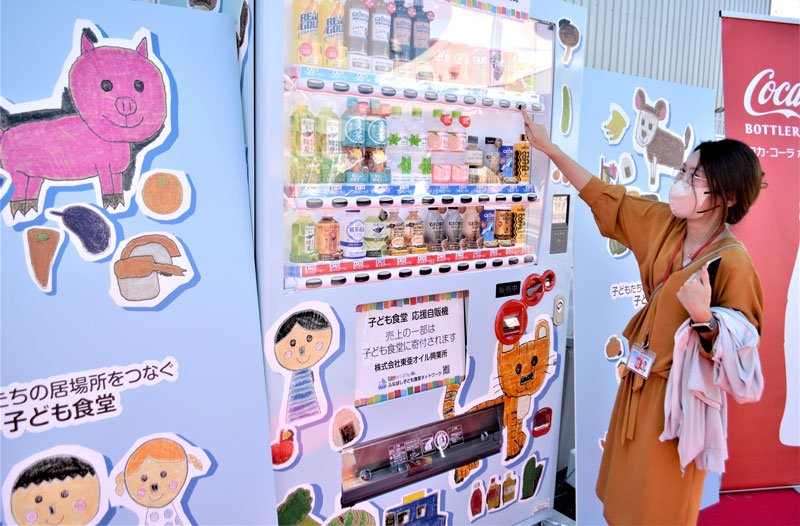 オリジナルの優しいイラストが包む「子ども食堂応援自販機」で早速、飲料を購入する社員

