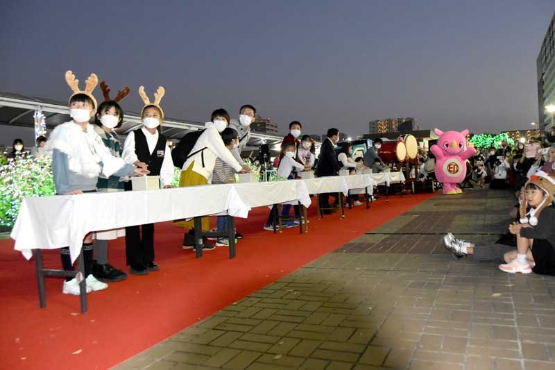 印西市の冬の風物詩として行われる沿線最大級のイルミネーションイベント「イルミライ★ＩＮＺＡＩ」の点灯式。今年は前年から１０万球増やし６０万球とするなど内容を一層充実し、安達さん（左から４人目）ら親子連れらも楽しんだ＝昨年１１月１２日、北総線の千葉ニュータウン中央駅前