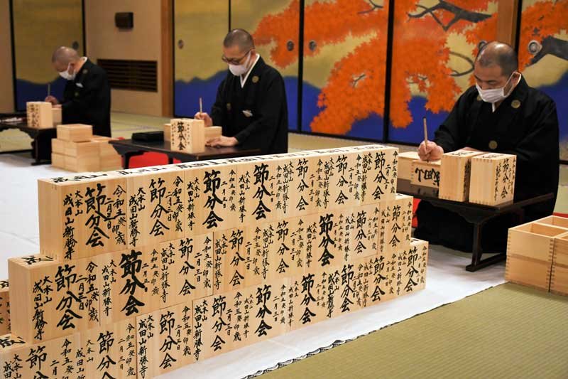 ２月３日の節分会で行う豆まきに向けて、福枡一つ一つに筆を入れる成田山新勝寺の僧侶＝１１日、成田市