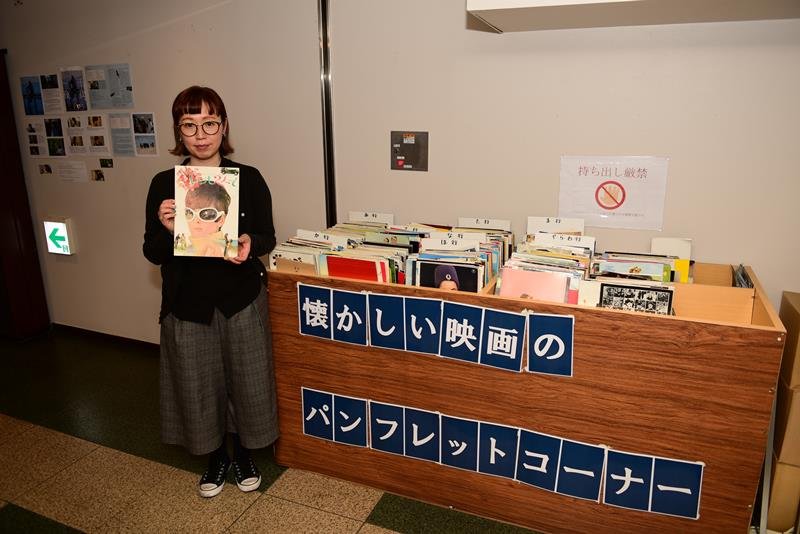 館内の映画パンフレットコーナーを紹介する山田さん。パンフレットは全て客からの寄付品＝柏市
