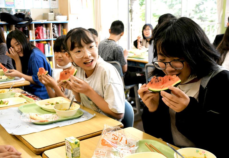 富里市特産のスイカをおいしそうに頬張る児童ら＝１３日、市立富里小学校