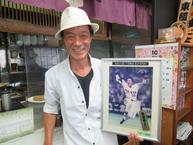 現役時代の阿部コーチがサヨナラホームランを打った際の写真を手にする宮崎さん。阿部コーチが店でサインした＝４日、浦安市
