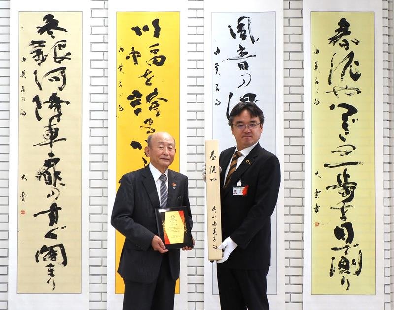 片山由美子さんの４句を書にした作品など計８幅を寄贈する辻元さん（左）＝袖ケ浦市
