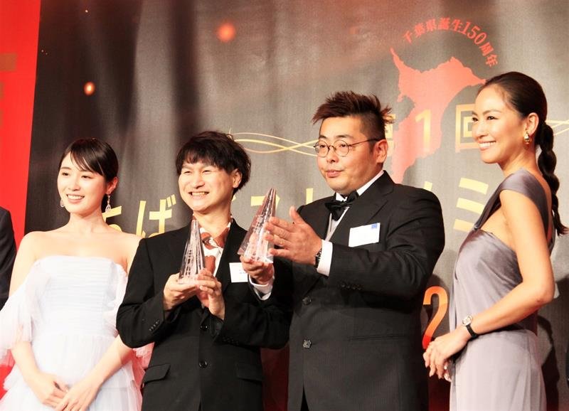 表彰式で大賞のトロフィーを掲げる杉岡さん（右から２人目）と須藤さん（同３人目）。左は南房総市出身のタレントでプレゼンターを務めた高山一実さん＝千葉市美浜区
