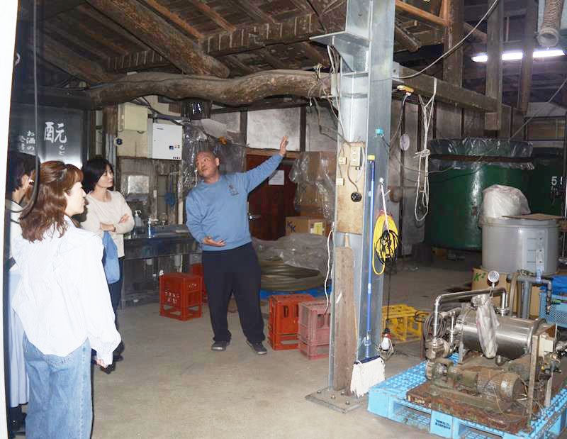 大きなタンクが並ぶ酒蔵の中を案内する守屋雅博さん（中央）＝山武市