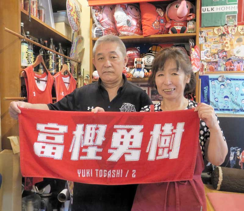 ジェッツのグッズであふれる店内で、富樫勇樹選手のタオルを掲げる今野勝夫さん（左）と今日子さん＝２日、船橋市習志野台のダイニングバー「Ｍａｍａ家」