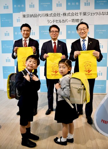 ジェッツのマスコットキャラクターが描かれたランドセルカバーを贈られた子どもたち（手前）＝市川市役所