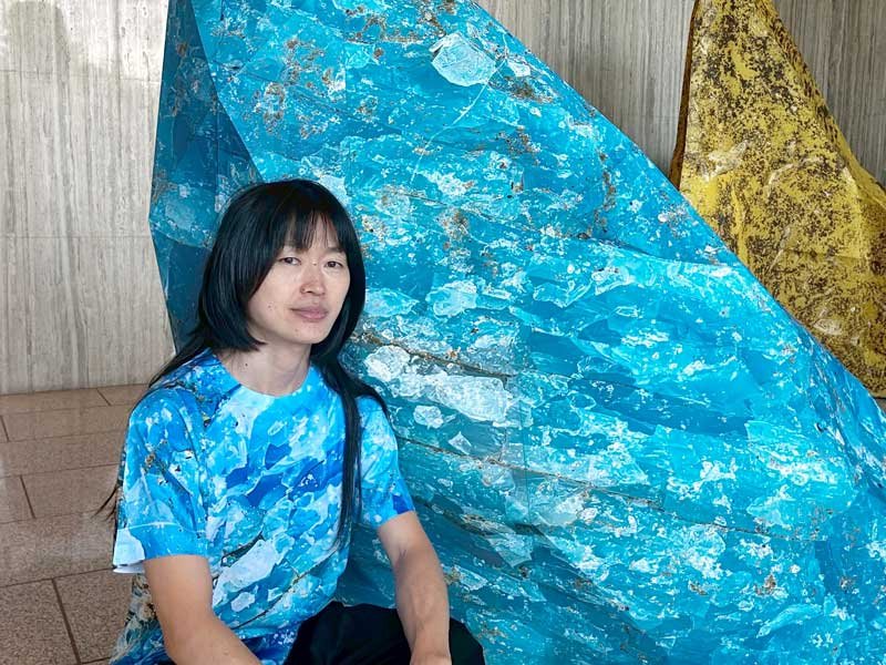 「ジャイアント・マイクロ・プラスチック」の前で自作のマイクロプラスチック柄のシャツを着る安西さん＝千葉市美浜区