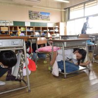 地震発生を想定した訓練で机の下に身を隠す児童
