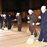 大本堂の広い畳を丁寧にはく僧侶と職員