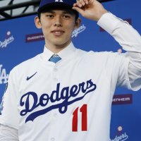 ドジャースの入団記者会見で、背番号１１のユニホームに袖を通し撮影に応じる佐々木朗希投手＝２２日、ロサンゼルス（共同）