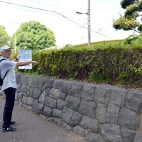 かつて高さ２００メートルの主塔が建っていた場所を示す山本会長。片側２車線の道路を挟んだ向かいの石垣の上に「船橋無線塔記念碑」が建てられている＝船橋市
